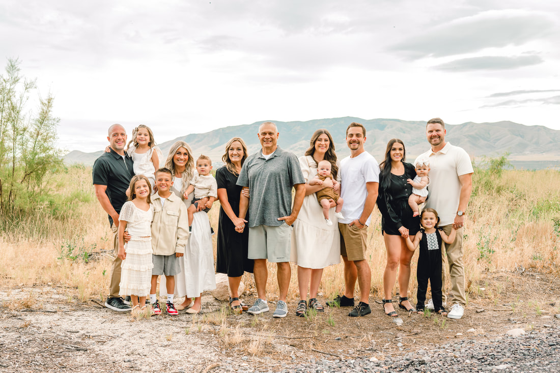 Extended family in neutral colors on a trail near Utah Lake with mountains in the background