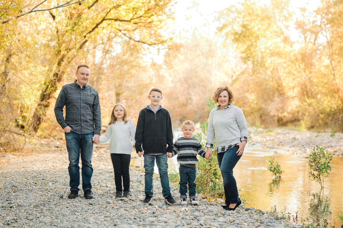 Family in neutral colors surrounded by fall foliage near a riverbed.