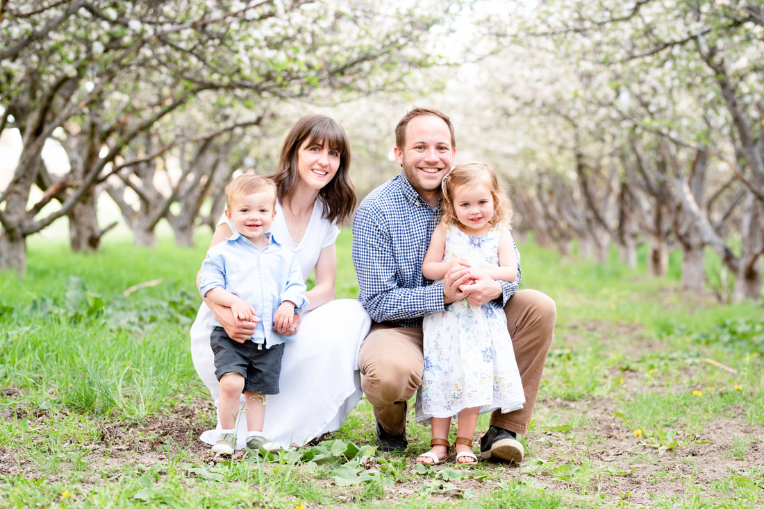 Family smiling in apple orchard and blossoms in Provo, UT