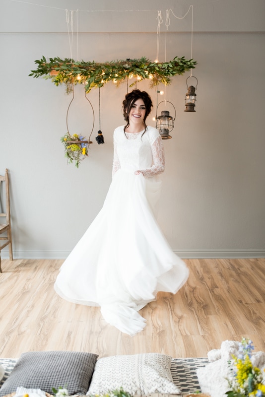 Rustic Wedding photoshoot includes bride in lace gown, greenery chandelier, hanging lanterns, pillow seats, and more.