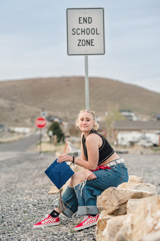 Graduating senior girl sits in front of end school zone sign