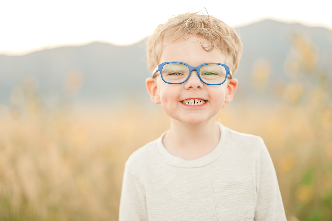 Little boy in blue glasses smiles into the camera during family photos.