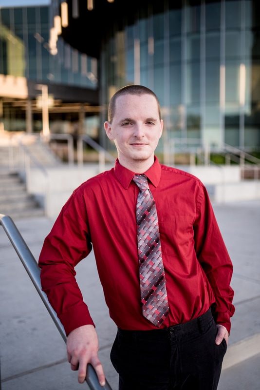 Photo of graduating senior in dress shirt and tie in front of modern glass and steel building