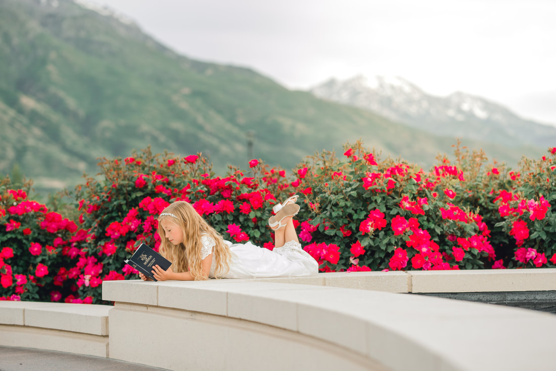 Girl reading scriptures in a white dress, surrounded by roses