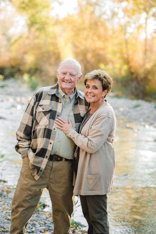 Elderly couple hold each other near a river with fall leaves