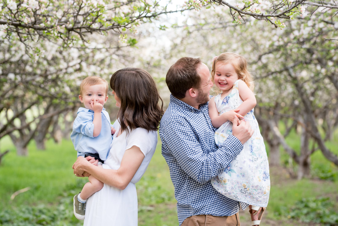 Family dressed in white and blue smiling and laughing in Utah apple orchard