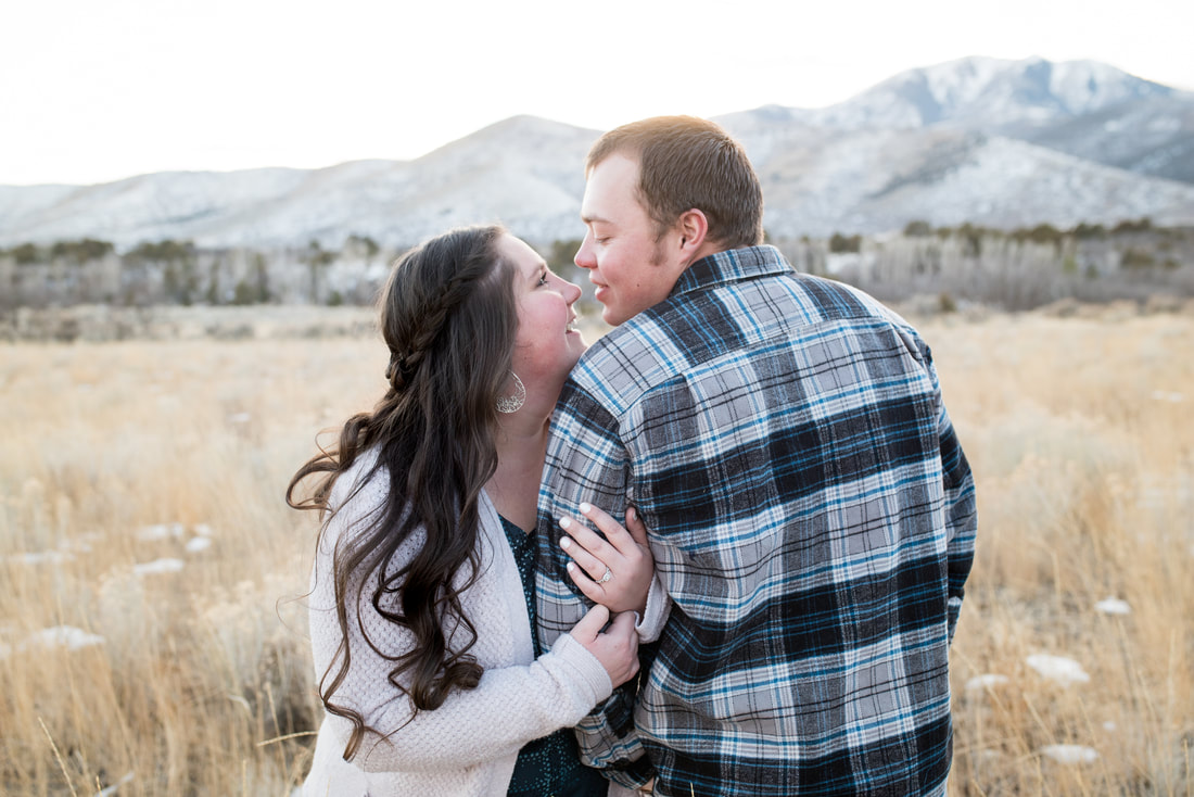 Engaged couple in golden field with snowy mountains in background