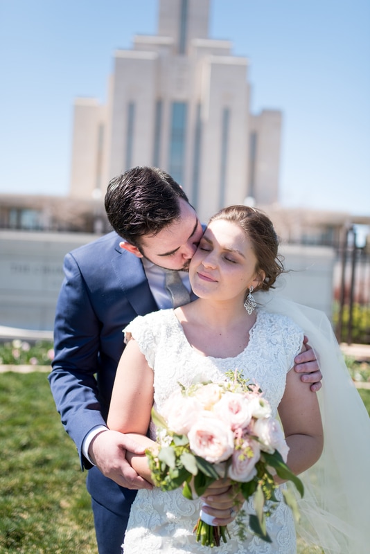 Groom kissing bride in front of Oquirrh mountain temple