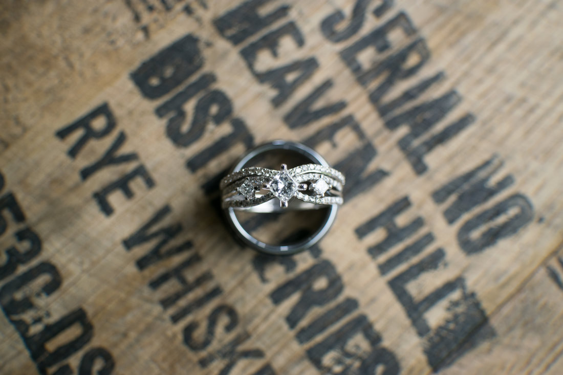 Bride's ring sits on groom's ring on top of a wine barrel