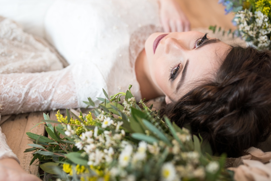  Boho bride lies among yellow and blue wildflowers.