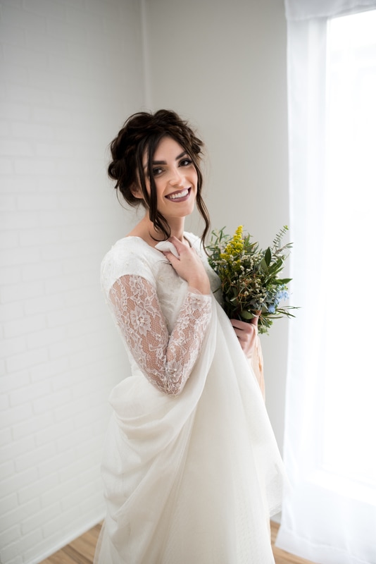 Beautiful young bride in white lace dress smiles and holds dress