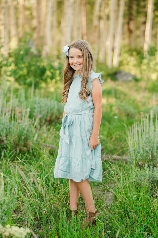 Cute little girl in blue dress surrounded by green grass and wildflowers in Utah